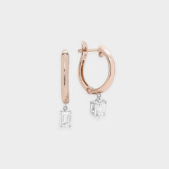 Rose gold hoop earrings with emerald-cut gemstones on a light gray background