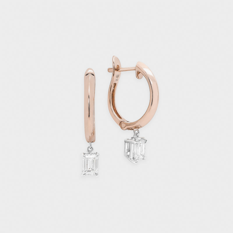 Rose gold hoop earrings with emerald-cut gemstones on a light gray background