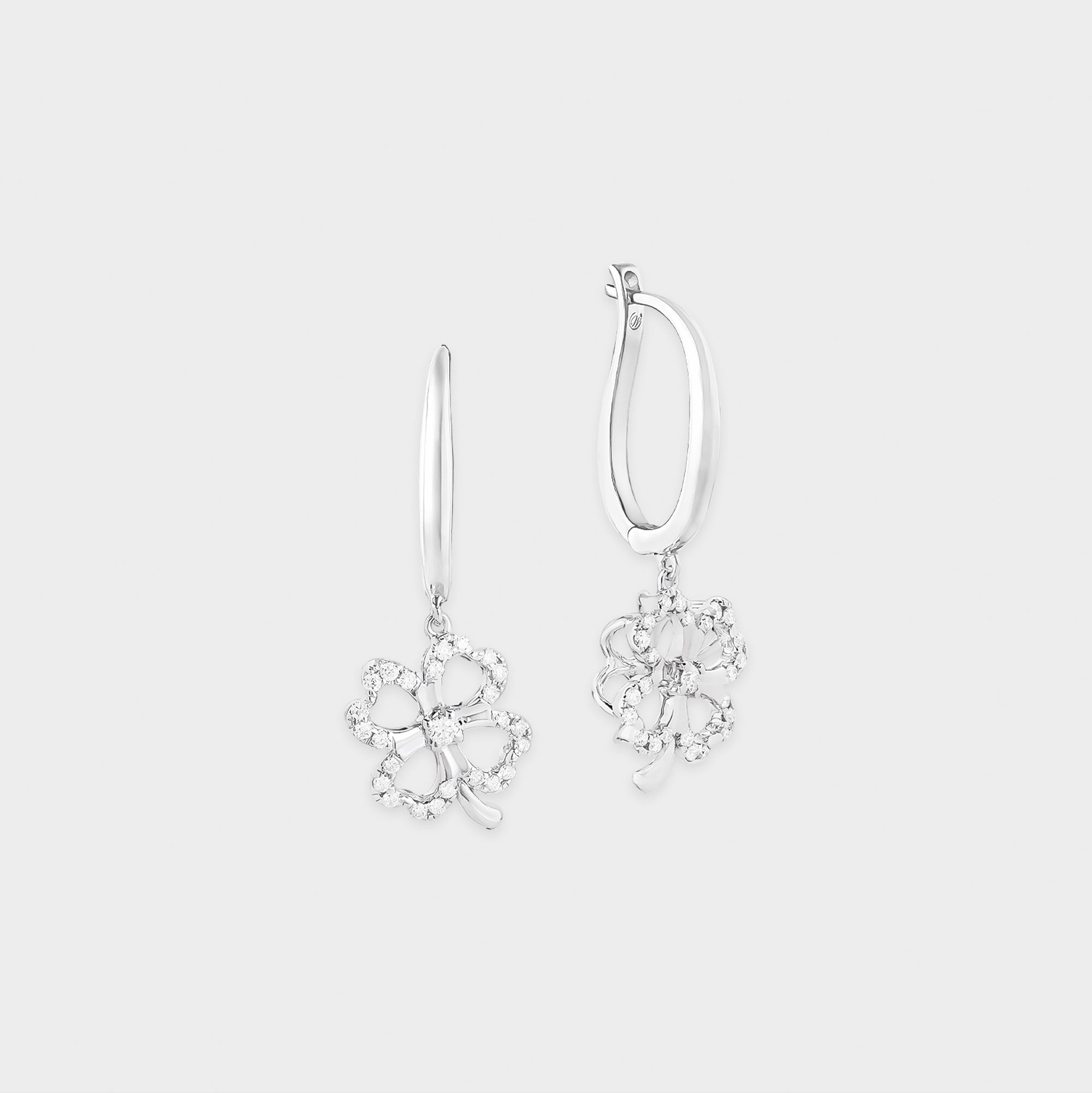 Pair of clover-shaped white gold earrings on a light gray background
