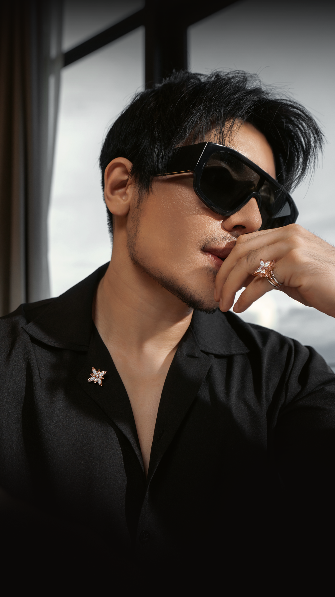 Man wearing sunglasses and a black shirt with a diamond star pin.